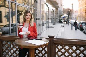 schön jung Geschäftsfrau mit ein Einweg Kaffee Tasse, Trinken Kaffee, und halten Tablette im ihr Hände gegen städtisch Stadt Hintergrund foto