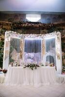 Hochzeit Dekor - - Frühling Blumen und Eukalyptus Geäst, Kerze Büchsen und lila Stoff im das Hochzeit Bogen auf das Hintergrund von Grün Gras und das Fluss. foto