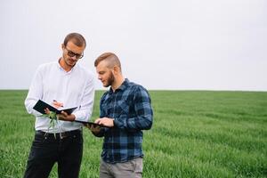 zwei Farmer Stehen im ein Grün Weizen Feld und Shake Hände foto