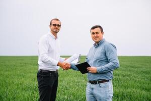zwei Farmer Stehen im ein Grün Weizen Feld und Shake Hände foto
