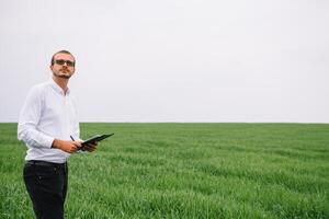 jung gut aussehend Agronom, Landwirtschaft Ingenieur Stehen im Grün Weizen Feld mit Tablette im Hände im früh Sommer. Landwirtschaft Konzept. foto