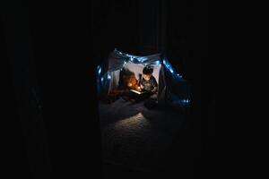 Kind Junge lesen mit Buch und Taschenlampe und Teddy Bär im Zelt. Vor gehen zu Bett. foto