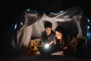 glücklich Familie Mutter und Kind Sohn lesen ein Buch mit ein Taschenlampe im ein Zelt beim heim. Familie Konzept. foto