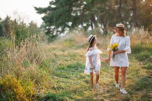 heiter Mutter und ihr wenig Tochter haben Spaß zusammen im das Sommer- Hintergrund. glücklich Familie im das Natur Hintergrund. süß Mädchen mit bunt Blumen foto