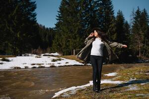 Frau im ein Hut und Grün Jacke ist ruhen auf das Natur im das Berge in der Nähe von das Berg Fluss. entspannen Zeit auf Urlaub Konzept Reise. foto