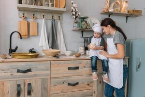 jung glücklich Mama und ihr Baby Koch Kekse beim Zuhause im das Küche. Weihnachten hausgemacht Lebkuchen. süß Junge mit Mutter im Weiß Uniform und Hut gekocht Schokolade Kekse foto