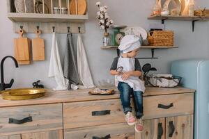 jung Junge süß auf das Küche Koch Koch im Weiß Uniform und Hut in der Nähe von Tisch. Weihnachten hausgemacht Lebkuchen. das Junge gekocht das Schokolade Kekse foto