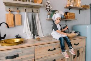 jung Junge süß auf das Küche Koch Koch im Weiß Uniform und Hut in der Nähe von Tisch. Weihnachten hausgemacht Lebkuchen. das Junge gekocht das Schokolade Kekse. foto