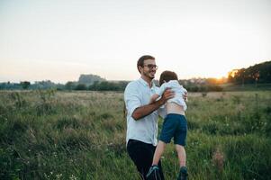 gut aussehend Papa mit seine wenig süß Sohn sind haben Spaß und spielen auf Grün grasig Rasen. glücklich Familie Konzept. Schönheit Natur Szene mit Familie draussen Lebensstil. Familie ruhen zusammen. Väter Tag. foto