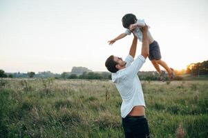 gut aussehend Papa mit seine wenig süß Sohn sind haben Spaß und spielen auf Grün grasig Rasen. glücklich Familie Konzept. Schönheit Natur Szene mit Familie draussen Lebensstil. Familie ruhen zusammen. Väter Tag. foto