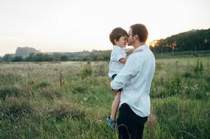 gut aussehend Papa mit seine wenig süß Sohn sind haben Spaß und spielen auf Grün grasig Rasen. glücklich Familie Konzept. Schönheit Natur Szene mit Familie draussen Lebensstil. Familie ruhen zusammen. Väter Tag. foto