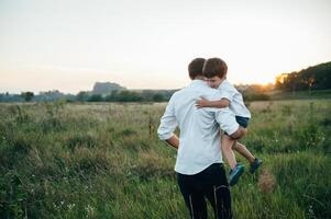 gut aussehend Papa mit seine wenig süß Sohn sind haben Spaß und spielen auf Grün grasig Rasen. glücklich Familie Konzept. Schönheit Natur Szene mit Familie draussen Lebensstil. Familie ruhen zusammen. Väter Tag. foto