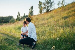 gut aussehend Papa mit seine wenig süß Sohn sind haben Spaß und spielen auf Grün grasig Rasen. glücklich Familie Konzept. Schönheit Natur Szene mit Familie draussen Lebensstil. Familie ruhen zusammen. Väter Tag. foto