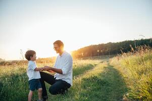 gut aussehend Papa mit seine wenig süß Sohn sind haben Spaß und spielen auf Grün grasig Rasen. glücklich Familie Konzept. Schönheit Natur Szene mit Familie draussen Lebensstil. Familie ruhen zusammen. Väter Tag. foto