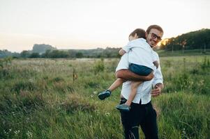 gut aussehend Papa mit seine wenig süß Sohn sind haben Spaß und spielen auf Grün grasig Rasen. glücklich Familie Konzept. Schönheit Natur Szene mit Familie draussen Lebensstil. Familie ruhen zusammen. Väter Tag. foto