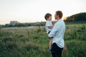 gut aussehend Papa mit seine wenig süß Sohn sind haben Spaß und spielen auf Grün grasig Rasen. glücklich Familie Konzept. Schönheit Natur Szene mit Familie draussen Lebensstil. Familie ruhen zusammen. Väter Tag. foto