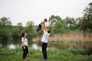 glücklich Familie Mutter Vater und Kind Sohn auf Natur auf Sonnenuntergang. Mutter, Papa und Kind Lachen und umarmen, genießen Natur außen. sonnig Tag, gut Stimmung. Konzept von ein glücklich Familie. foto