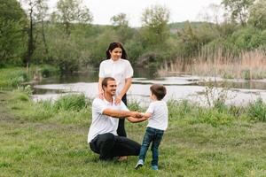 glücklich Familie Mutter Vater und Kind Sohn auf Natur auf Sonnenuntergang. Mutter, Papa und Kind Lachen und umarmen, genießen Natur außen. sonnig Tag, gut Stimmung. Konzept von ein glücklich Familie. foto