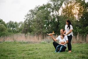 Vater, Mutter und Sohn spielen mit Spielzeug Flugzeug im das Park. freundlich Familie. Menschen haben Spaß draußen. Bild gemacht auf das Hintergrund von das Park und Blau Himmel. Konzept von ein glücklich Familie foto