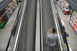 ein Mann mit ein Einkaufen Wagen auf ein Rolltreppe im ein Hardware- speichern. foto