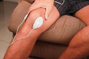 Mann mit ein Elektro Therapie Massagegerät oder Zehner Einheit auf seine Knie zum Schmerzen Linderung von Muskeln und Joint foto