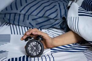 Frist und Zeit Verwaltung Konzept. Mann Hände halten schwarz Alarm Uhr auf Bett. Zeit zu aufwachen oben zum das Morgen Routine foto