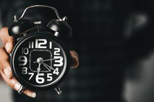 Zeit Verwaltung Konzept. Mann Hände halten schwarz retro Alarm Uhr. Zeit zu aufwachen oben zum das Morgen Routine foto