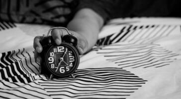 Frist und Zeit Verwaltung Konzept. Mann Hände halten schwarz Alarm Uhr auf Bett. Zeit zu aufwachen oben zum das Morgen Routine foto