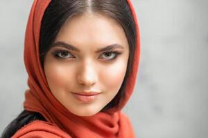 Porträt von ein ziemlich jung kaukasisch Frau mit bilden im ein rot Kopftuch auf grau Hintergrund. foto