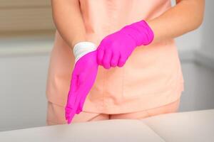 Hand von Kosmetikerin setzt auf steril Rosa Handschuhe bereitet vor zu erhalten Kunden drinnen. foto