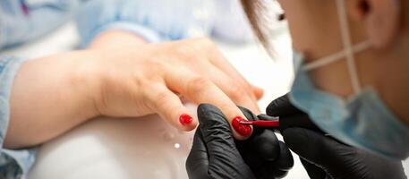 Gemälde Nägel von ein Frau. Hände von Maniküre im schwarz Handschuhe bewirbt sich rot Nagel Polieren auf weiblich Nägel im ein Schönheit Salon. foto