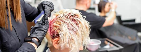 das Fachmann Friseur Verwendet ein Bürste zu anwenden das Rosa Farbstoff zu das Haar. Haar Färbung Konzept. foto