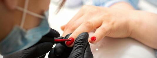 Gemälde Nägel von ein Frau. Hände von Maniküre im schwarz Handschuhe bewirbt sich rot Nagel Polieren auf weiblich Nägel im ein Schönheit Salon. foto
