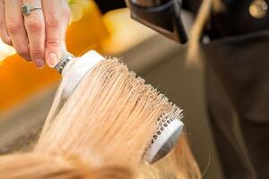 Friseur Hand Trocknen blond Haar mit ein Fön und runden Bürste im ein Schönheit Salon. foto