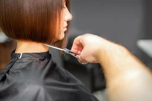 Frau haben ein Neu Haarschnitt. männlich Friseur Schneiden braun Haar mit Schere im ein Haar Salon. foto