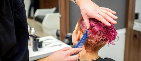 Hände von Friseur Kämmen Haar Herstellung kurz Rosa Frisur zum ein jung kaukasisch Frau im ein Schönheit Salon. foto