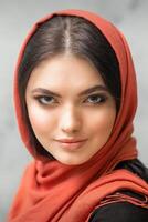 Porträt von ein ziemlich jung kaukasisch Frau mit bilden im ein rot Kopftuch auf grau Hintergrund. foto