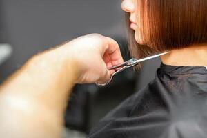 Frau haben ein Neu Haarschnitt. männlich Friseur Schneiden braun Haar mit Schere im ein Haar Salon. foto