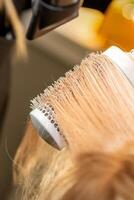 Friseur Hand Trocknen blond Haar mit ein Fön und runden Bürste im ein Schönheit Salon. foto