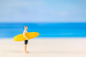 Miniatur Menschen Mann im ein Badeanzug, und halten ein Gelb Surfbrett auf das Strand foto