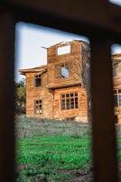 hölzern Haus mit gebrochen Fenster und ein groß Hof bewachsen mit Gras. foto