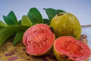 Guave isoliert. Sammlung von rot fleischig Guave Obst mit gelblich Grün Haut und Blätter isoliert auf ein Weiß Hintergrund mit Bambus Matten. foto