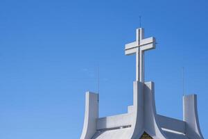 niedrig Winkel Aussicht von groß Kreuz auf Dach von Weiß Kirche gegen Blau Himmel Hintergrund foto