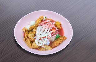 Yentafo Meeresfrüchte klein eben Nudel mit viele von knusprig gebraten Belag im Rosa Oval Schüssel auf hölzern Tabelle Spitze, asiatisch Straße Essen Stil foto