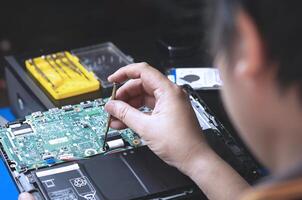 selektiv Fokus beim Schraubendreher im Techniker Hand, Rückseite Seite von Techniker ist Montage das Hauptplatine von Laptop Computer beim Werkstatt foto