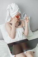 Twer, Russland-August 2, 2021 ein Frau nach ein Dusche ist Lügen auf das Couch mit ein Laptop und ein Auge Maske beim das gleich Zeit. das Konzept von Multitasking im das einundzwanzigster Jahrhundert. foto