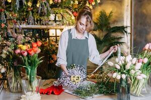 ein Frau im ihr Florist Geschäft sammelt Blumensträuße von Blumen. das Konzept von ein klein Geschäft. Blumensträuße von Tulpen zum das Urlaub auf März 8. foto