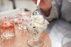 Löffel im Hand Schaufeln Eis Sahne von ein Glas Tasse mit ein Glas von Wasser foto