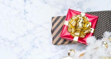 Blick von oben auf die rote glänzende Geschenkbox mit goldener Schleife und Band lag unter weißem Weihnachtsbaum auf weißem Marmor foto