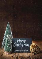 Frohe Weihnachten und ein glückliches neues Jahr auf Tafel mit Weihnachtsbaum und goldenem Tannenzapfen und Schneefall